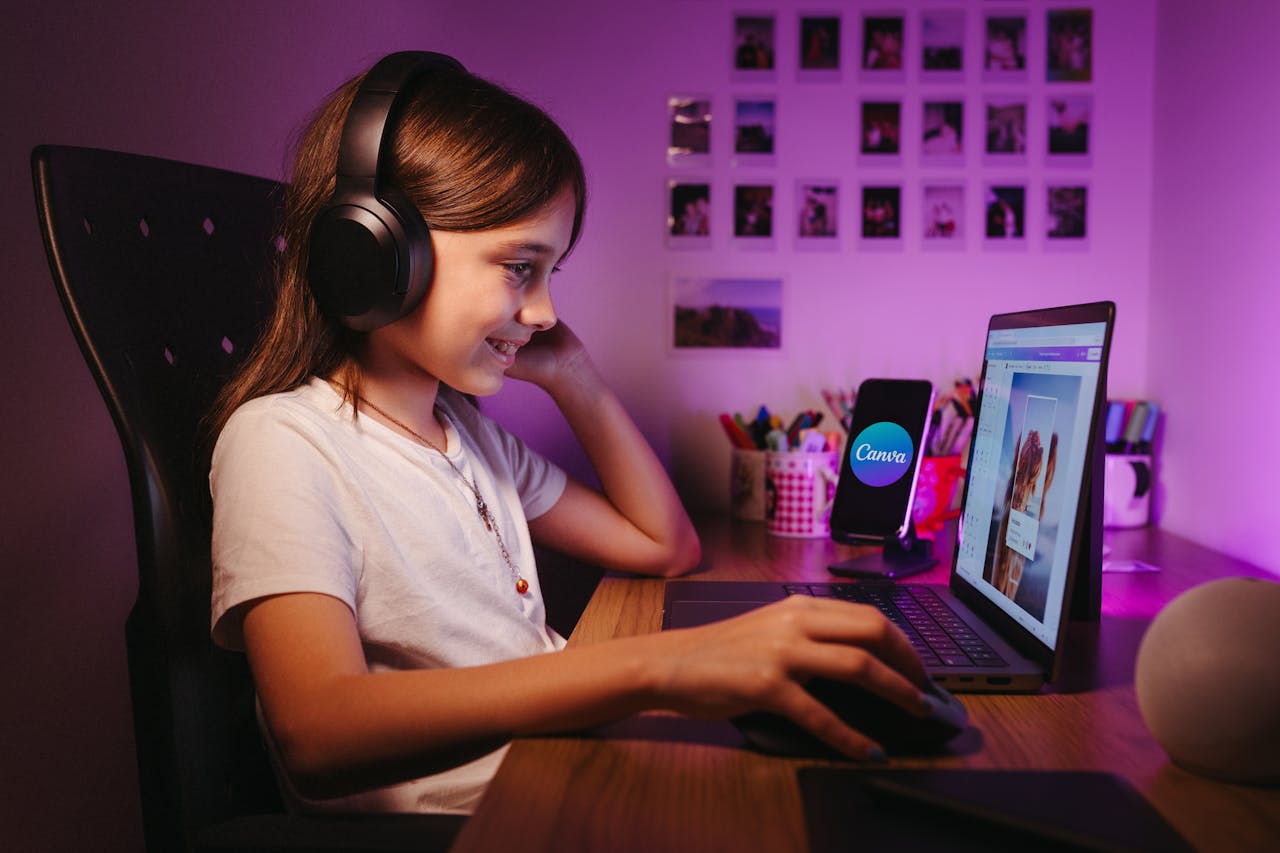 services-02 A young girl in headphones smiles while working on a laptop at a desk in a cozy room.